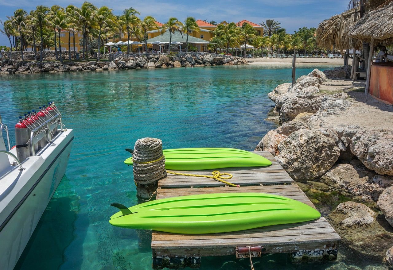 Kayaks on a small dock in a turquoise resort lagoon with palm trees and guest buildings on the far shore