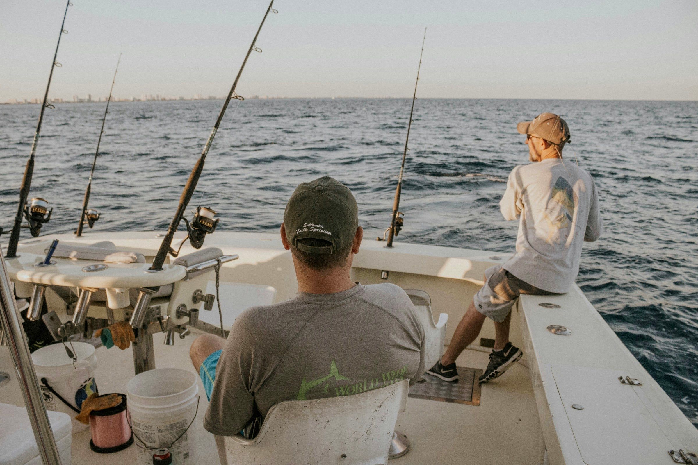 Two people on the back deck of a charter fishing boat with rods rigged over open water
