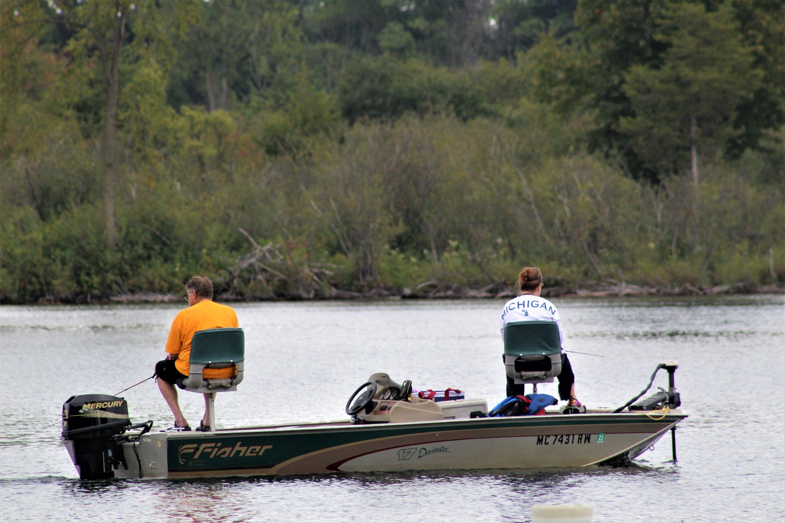 Two anglers casting from a bass boat along a wooded shoreline