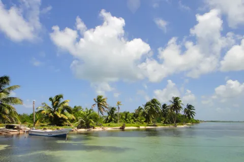 Clear, pale-green shallows and a palm-lined caye beside Turneffe Atoll with a skiff moored off the beach