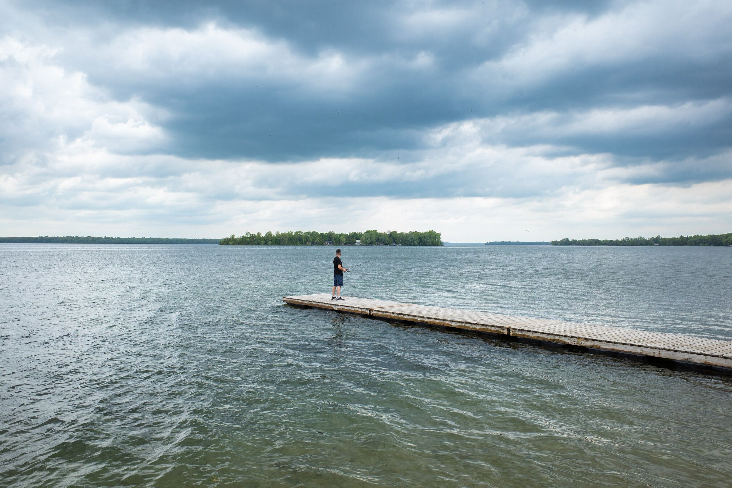 An angler casting from the end of a dock on Lake Couchiching under a stormy sky