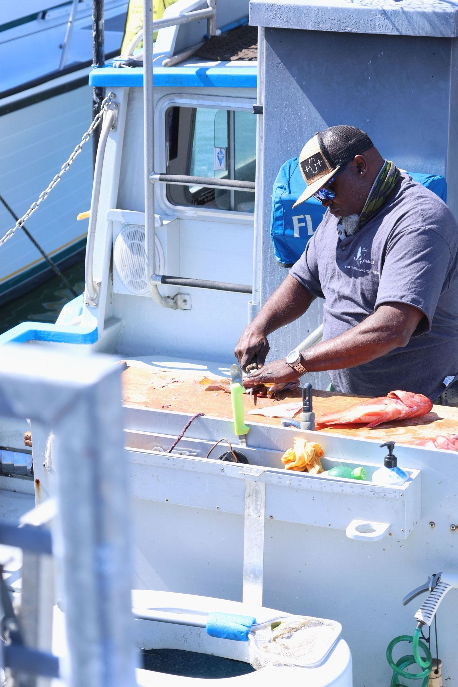 A deckhand in a cap and sunglasses fillets red fish on the cleaning table of a docked fishing boat in San Francisco