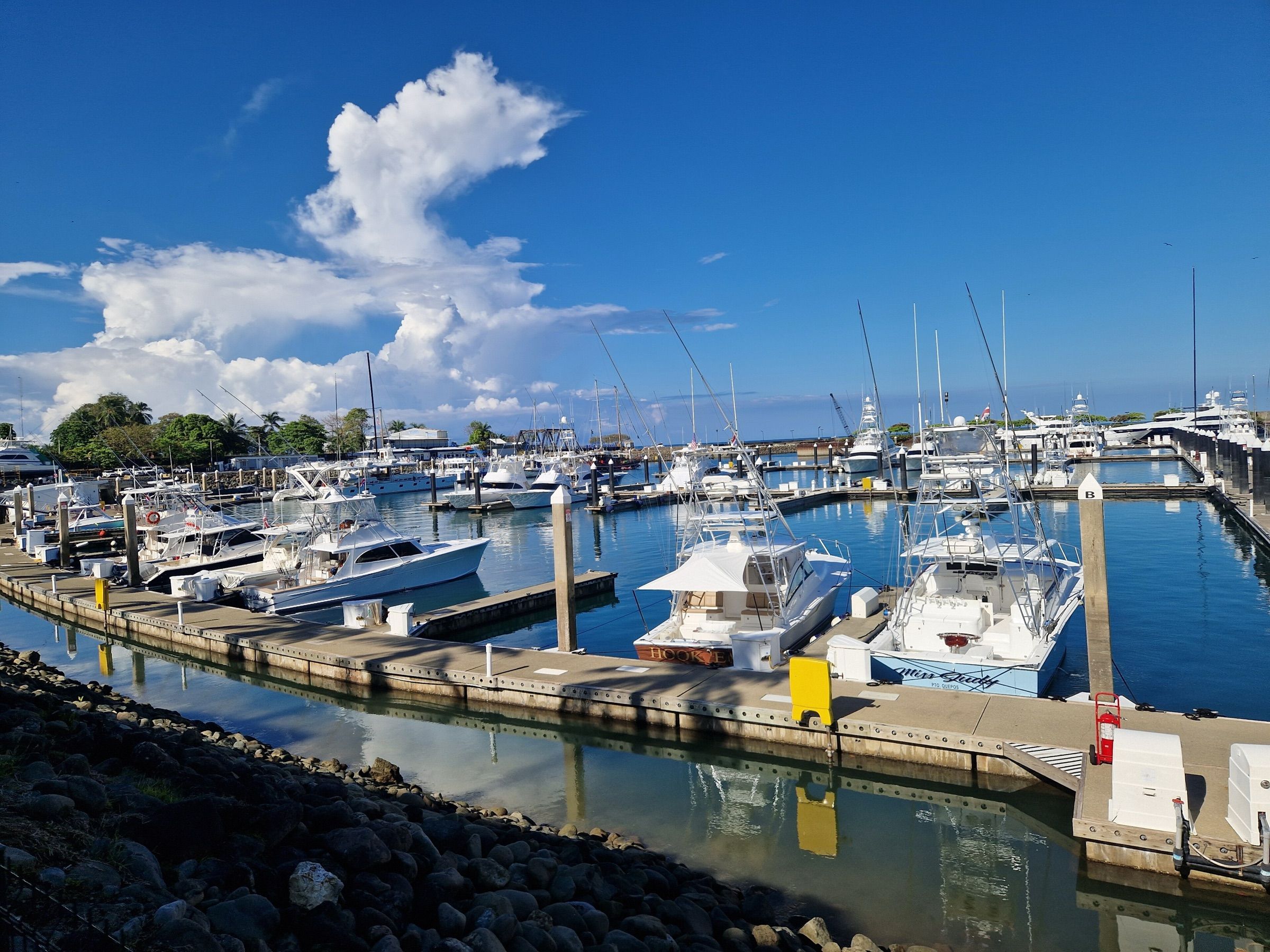 Sportfishing boats with tuna towers docked at Quepos Marina under a big white cloud