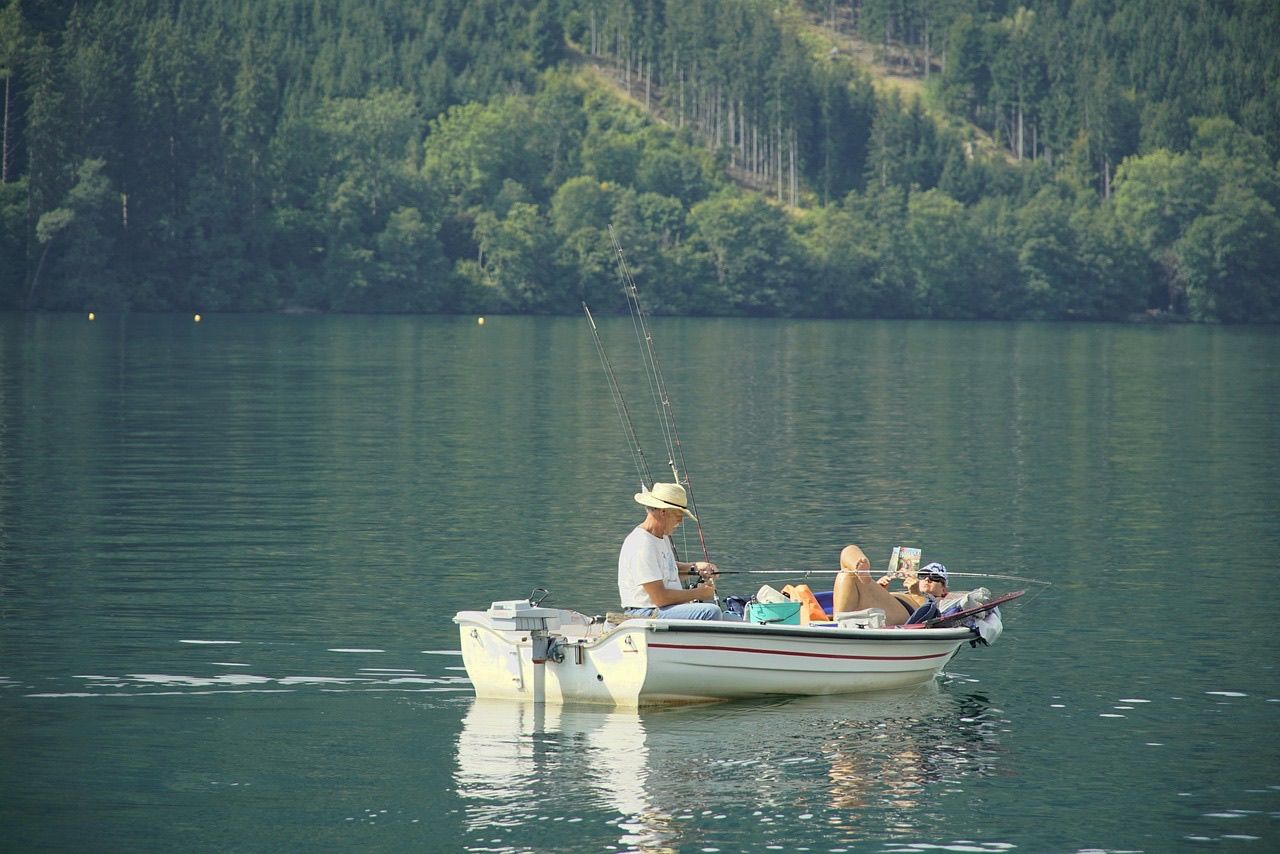 A man in a straw hat and a woman relaxing in a small fishing boat with rods out on a calm green lake