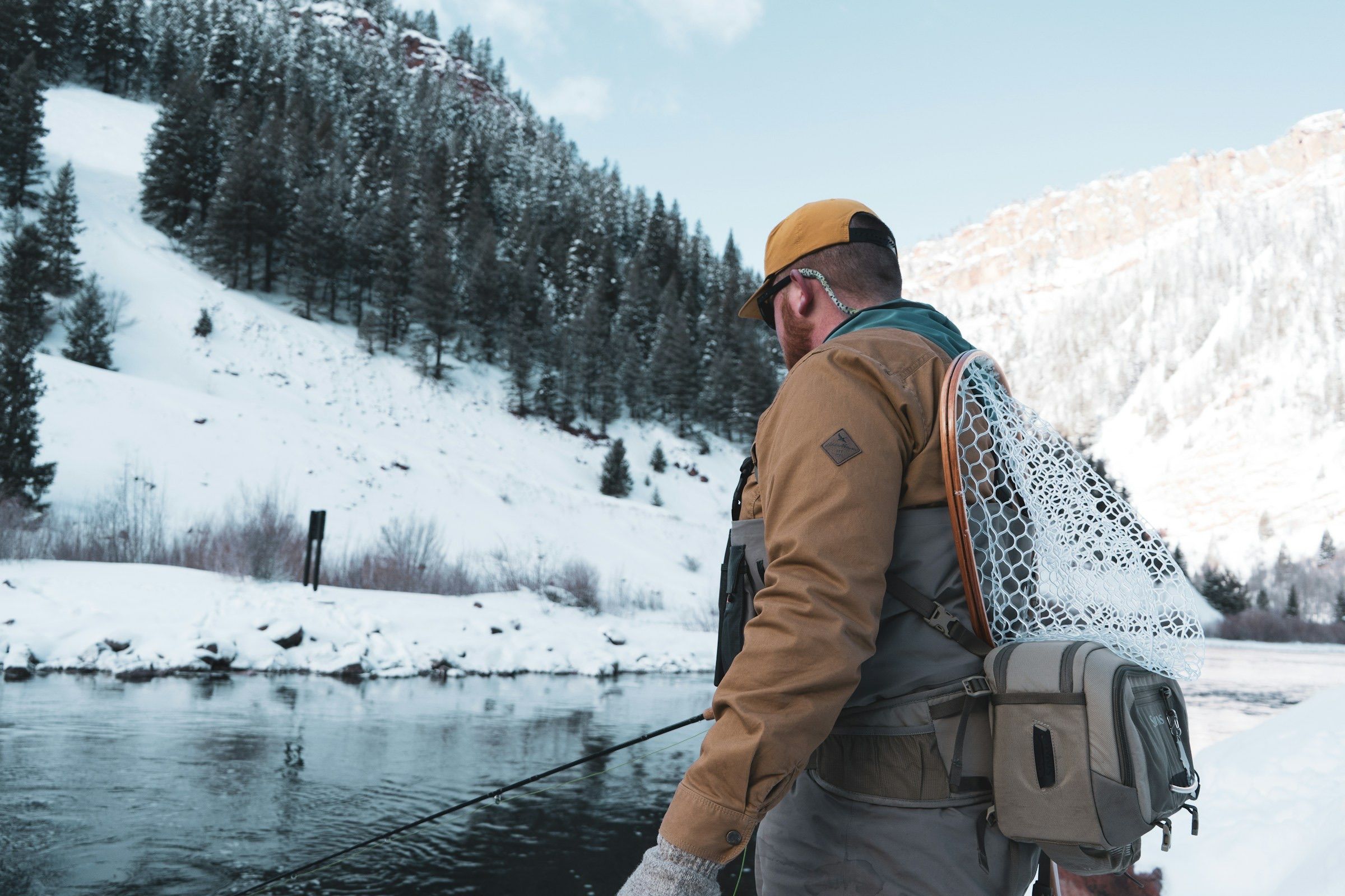 Fly angler with a landing net beside a river in deep winter snow