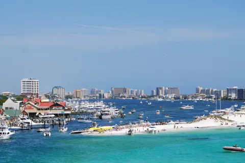 Destin Harbor packed with charter and pleasure boats beside a white-sand point and emerald water, with high-rise condos beyond