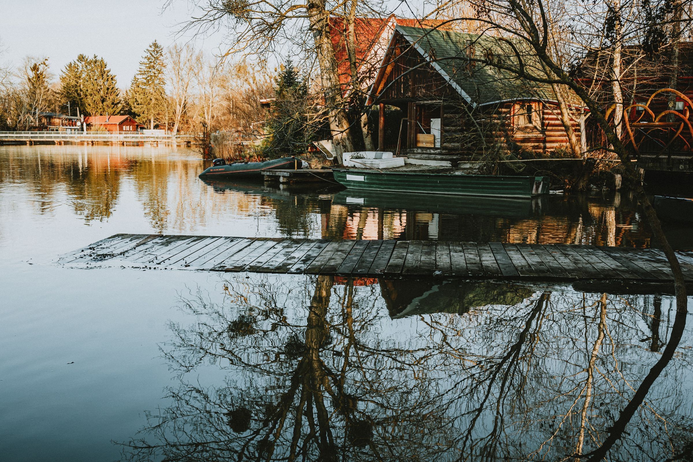 Wooden cabins and small boats along a still lake with a low pier in the foreground