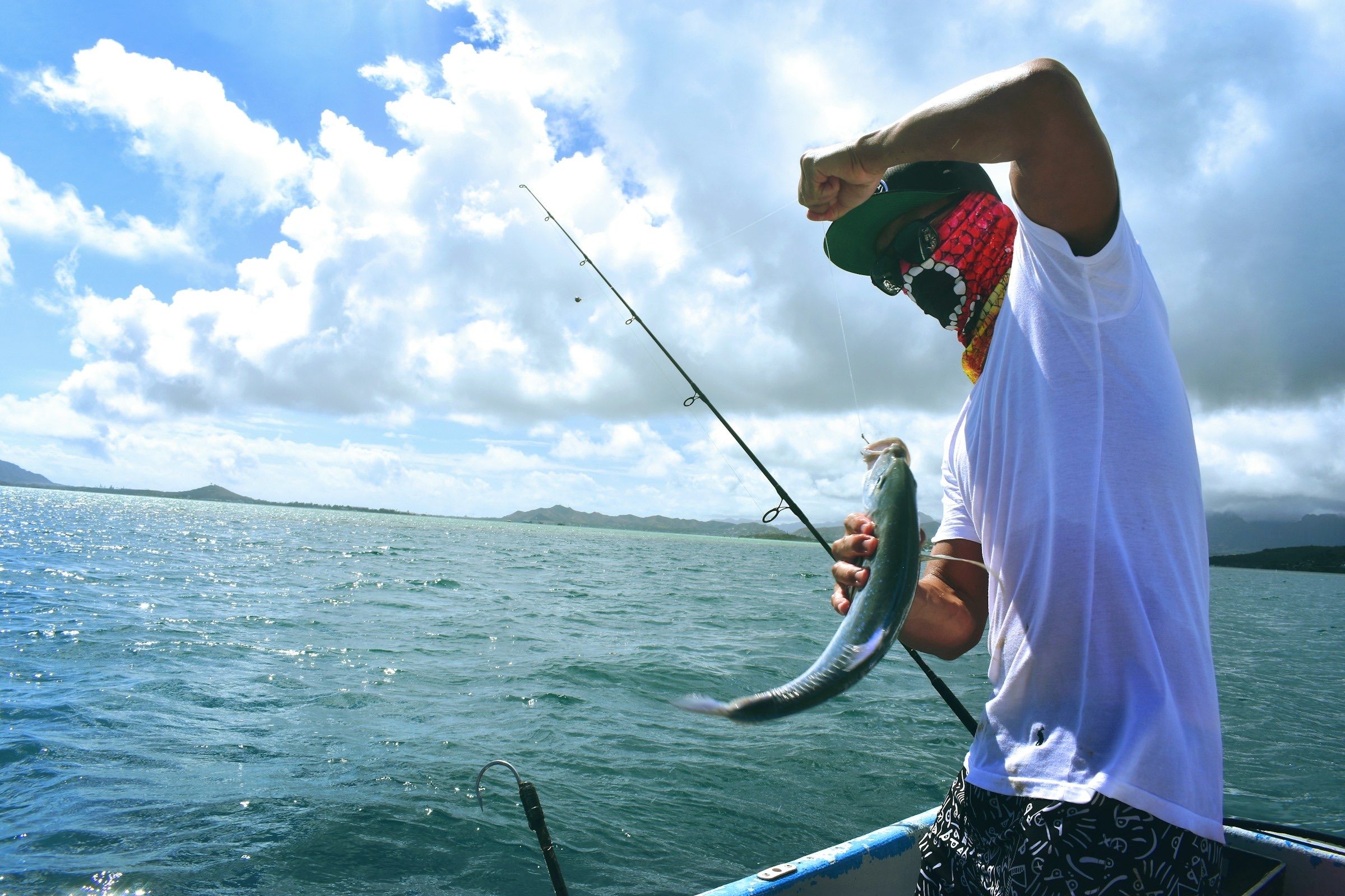 Angler on a boat lifting a fish from blue tropical water under puffy clouds