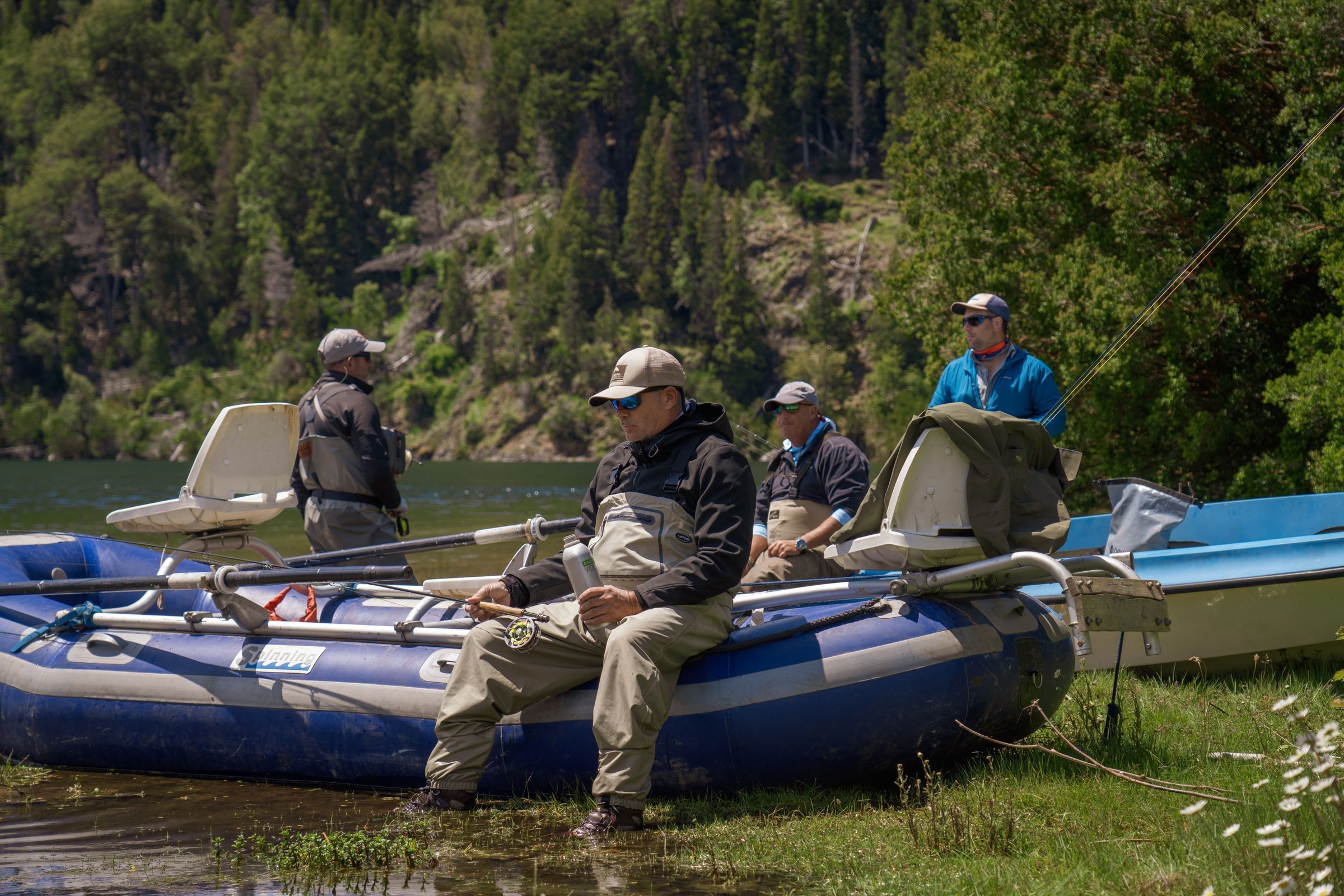 Fishing guides and anglers in waders gather beside inflatable drift boats on a lakeshore in Patagonia