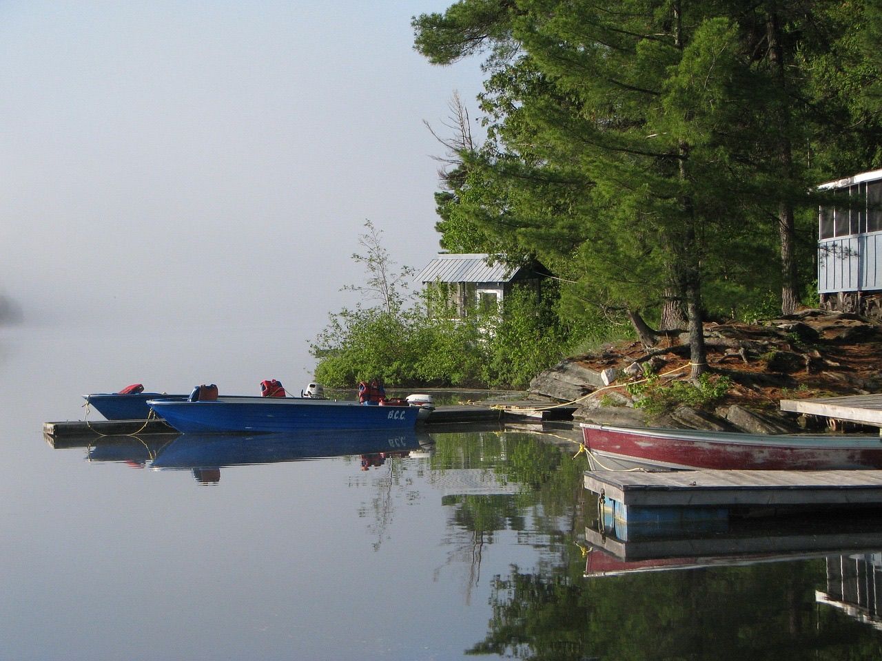 Fishing boats moored at docks below lakeside cabins on a misty, calm morning