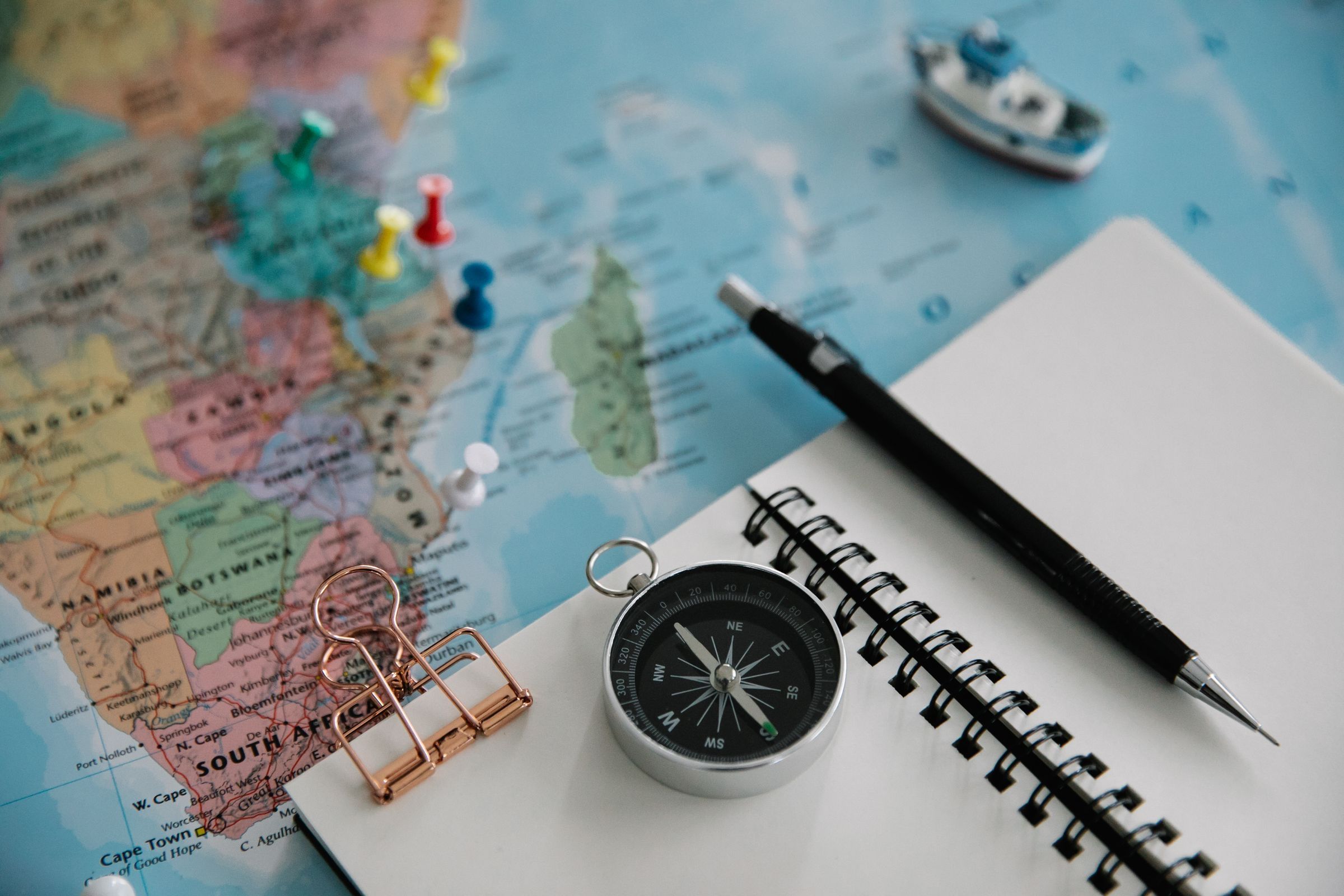 Trip planning flat lay of a pinned map, compass, notebook and pen