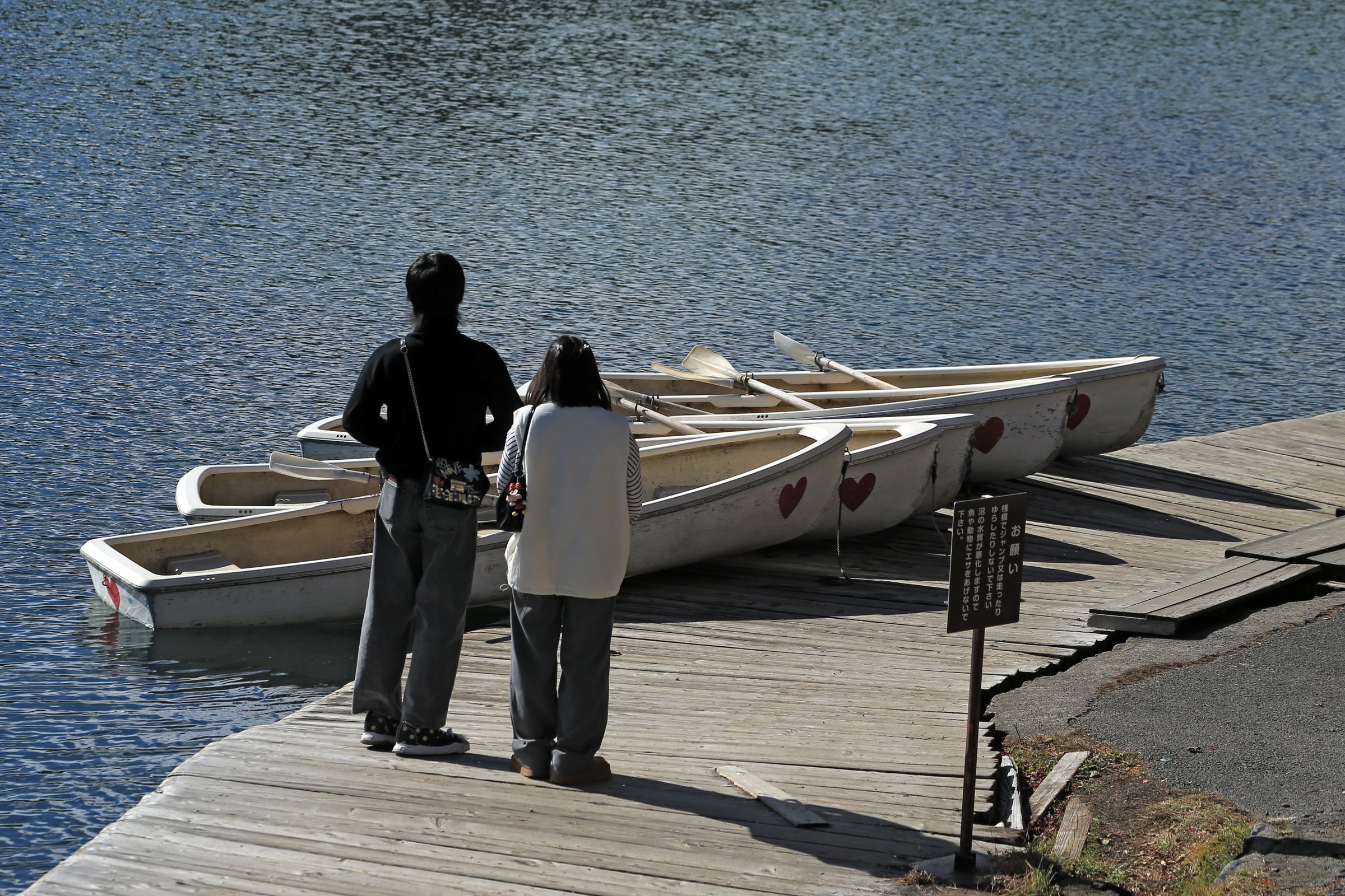 A couple stands together on a wooden dock beside rowboats tied up on a lake