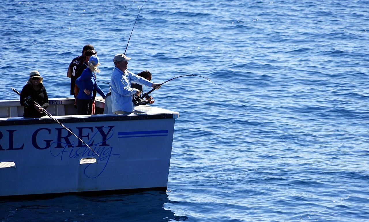 A group of anglers casting rods off the side of a charter boat on open blue sea