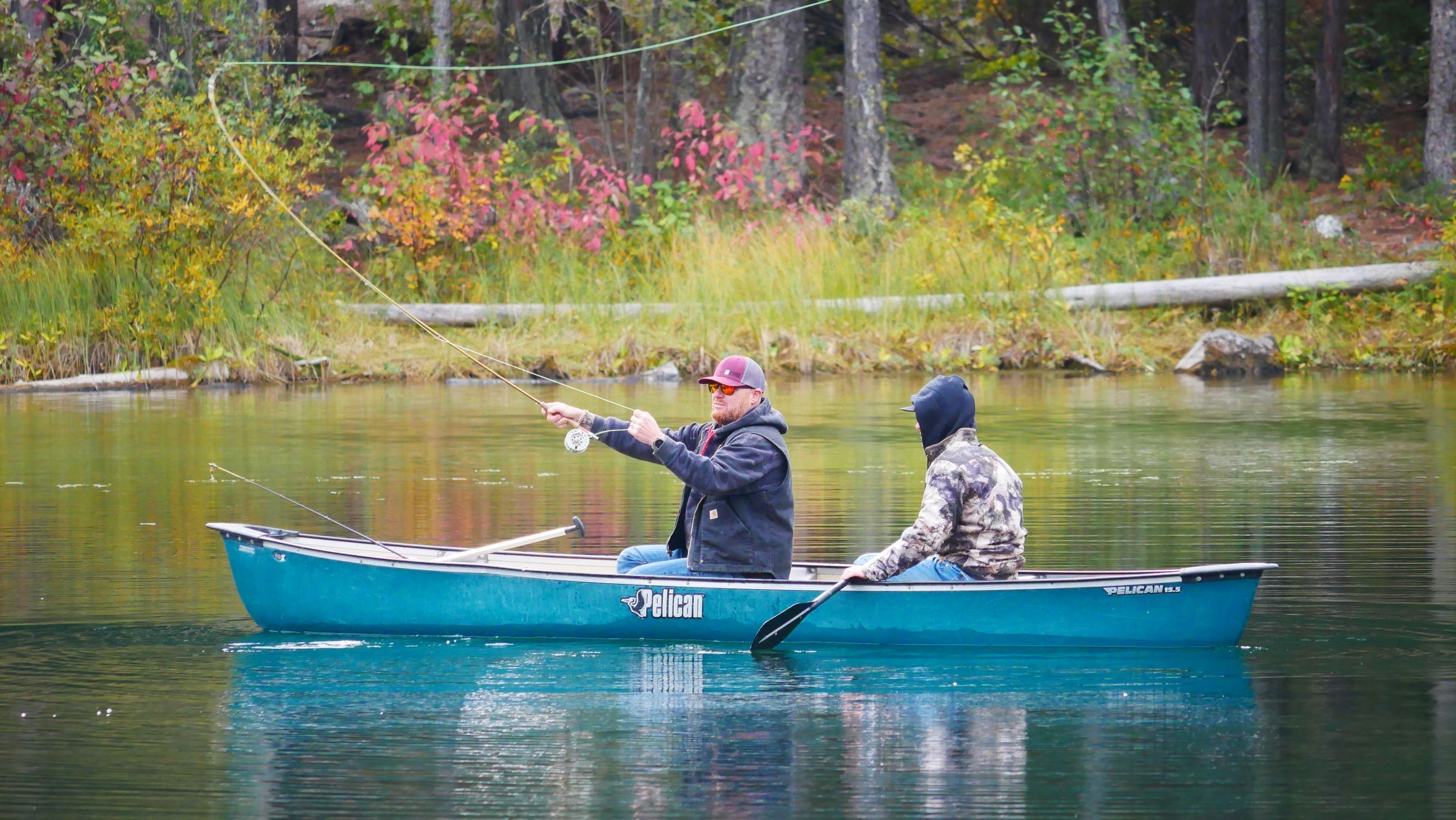 Two anglers fishing on their own from a canoe on a lake lined with autumn color in Canal Flats, British Columbia