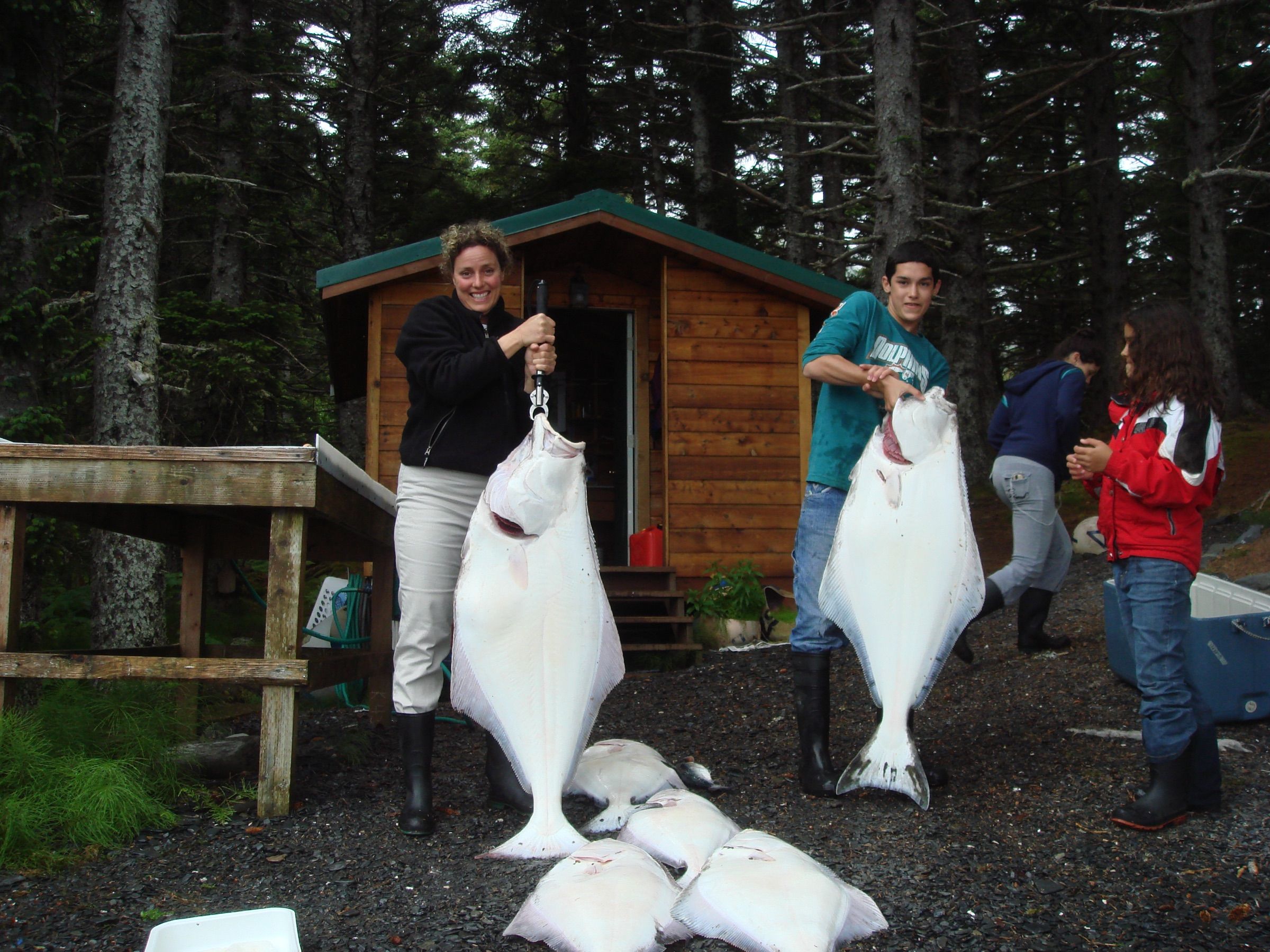 Anglers holding up large halibut outside a cabin