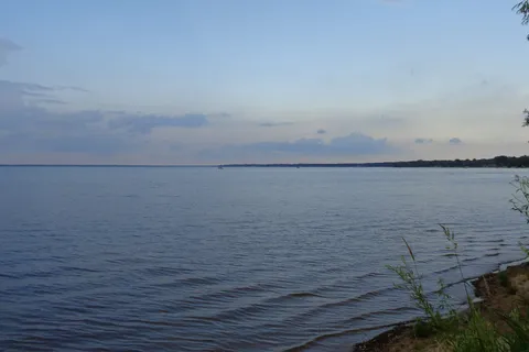 Calm open water of Houghton Lake at dusk with a wooded far shore and grasses in the foreground