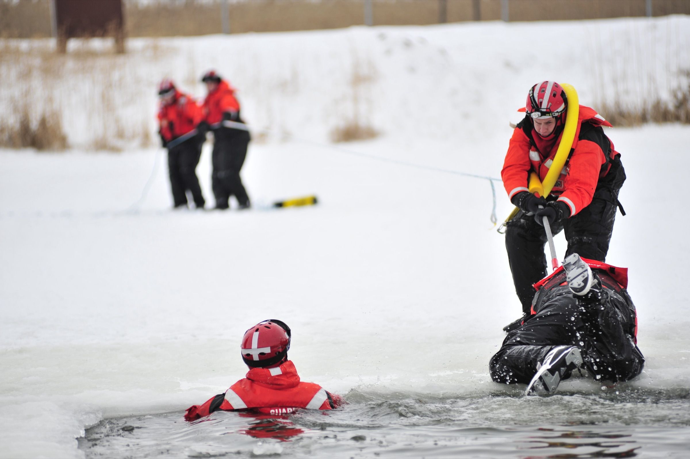 Coast Guard crew members practice pulling a person from open water through a hole in the ice during ice-rescue training