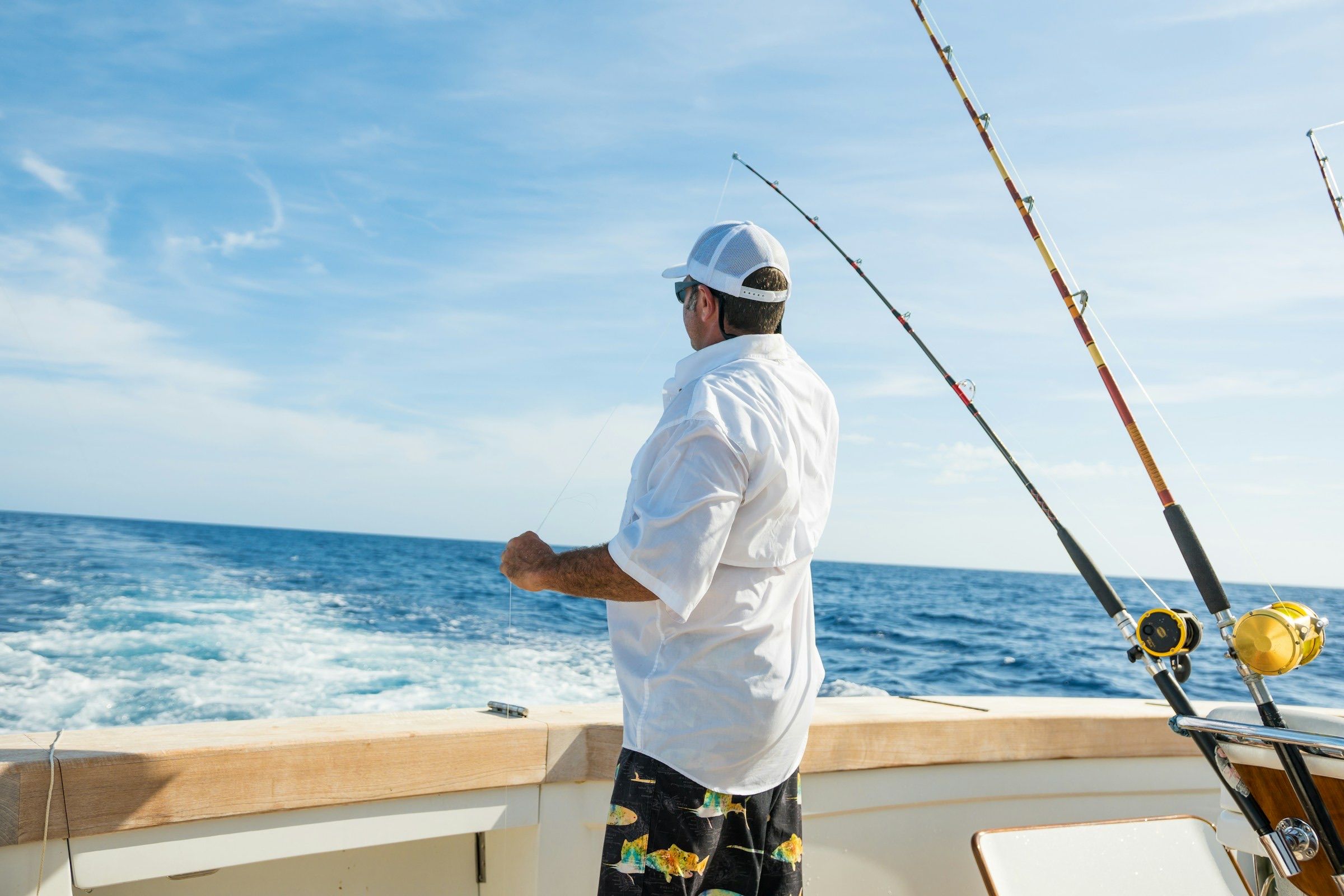 Angler on the deck of an offshore boat beside trolling rods on open blue water