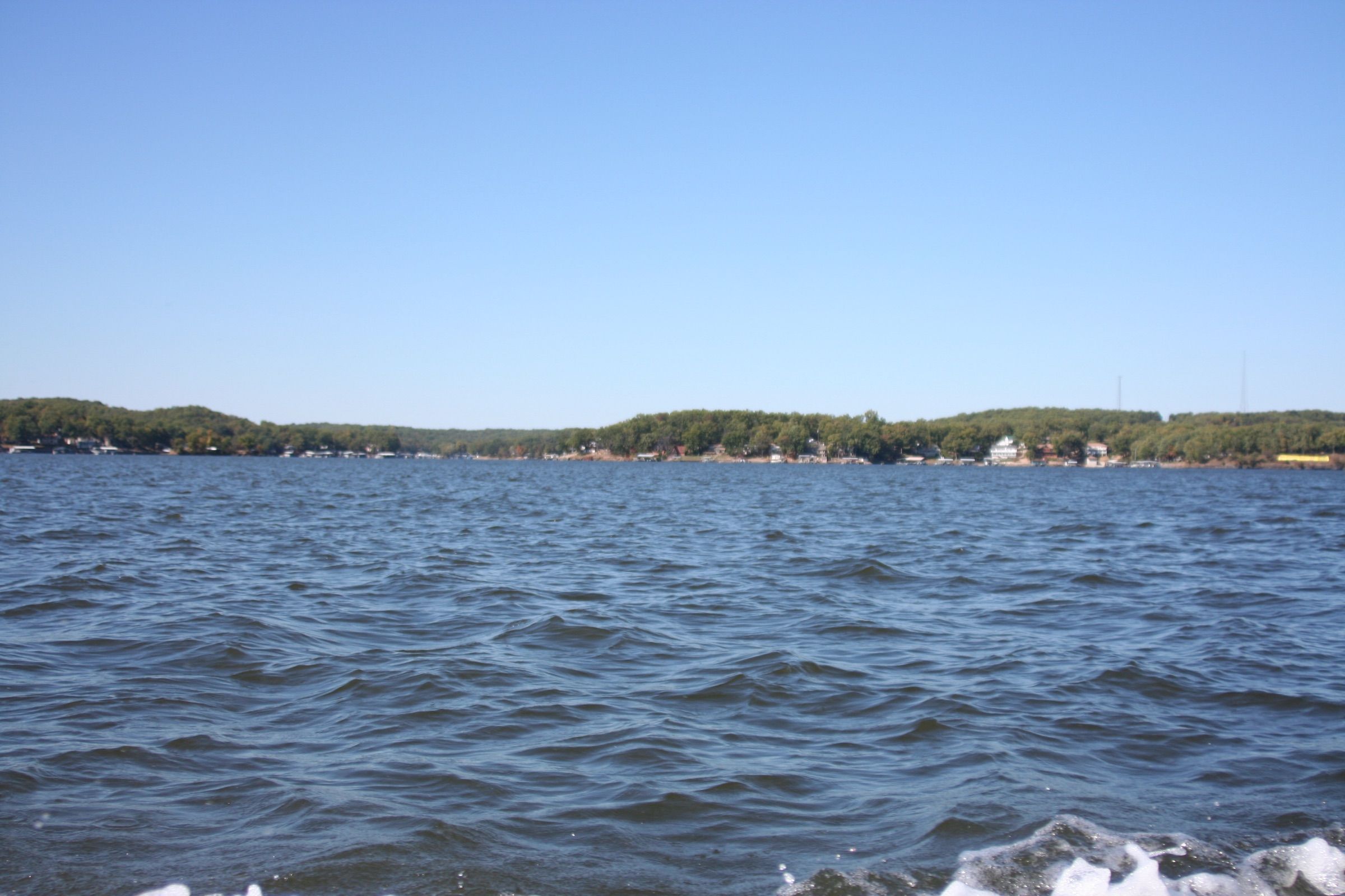 Open water on Lake of the Ozarks with lake homes and docks along a wooded shoreline