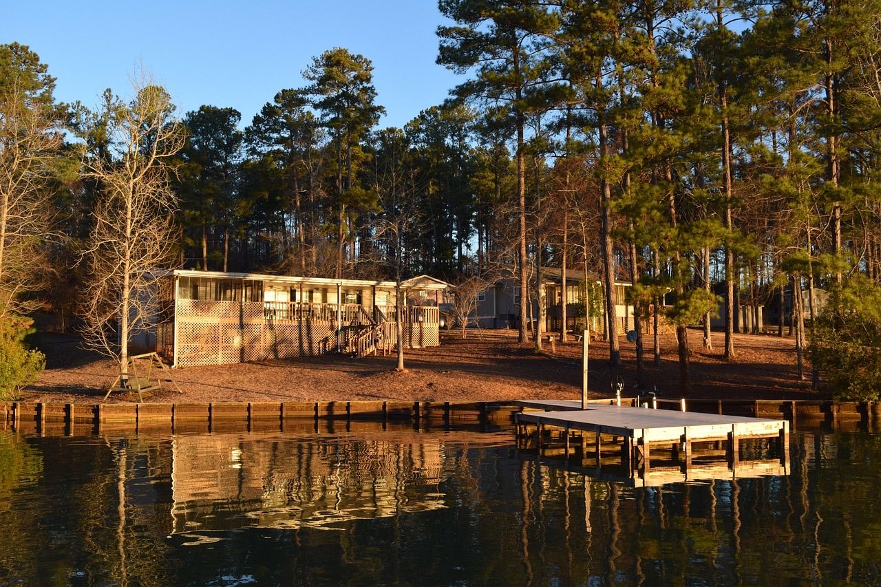 A lakeside cabin among tall pines with a private dock reflected in calm water at sunset