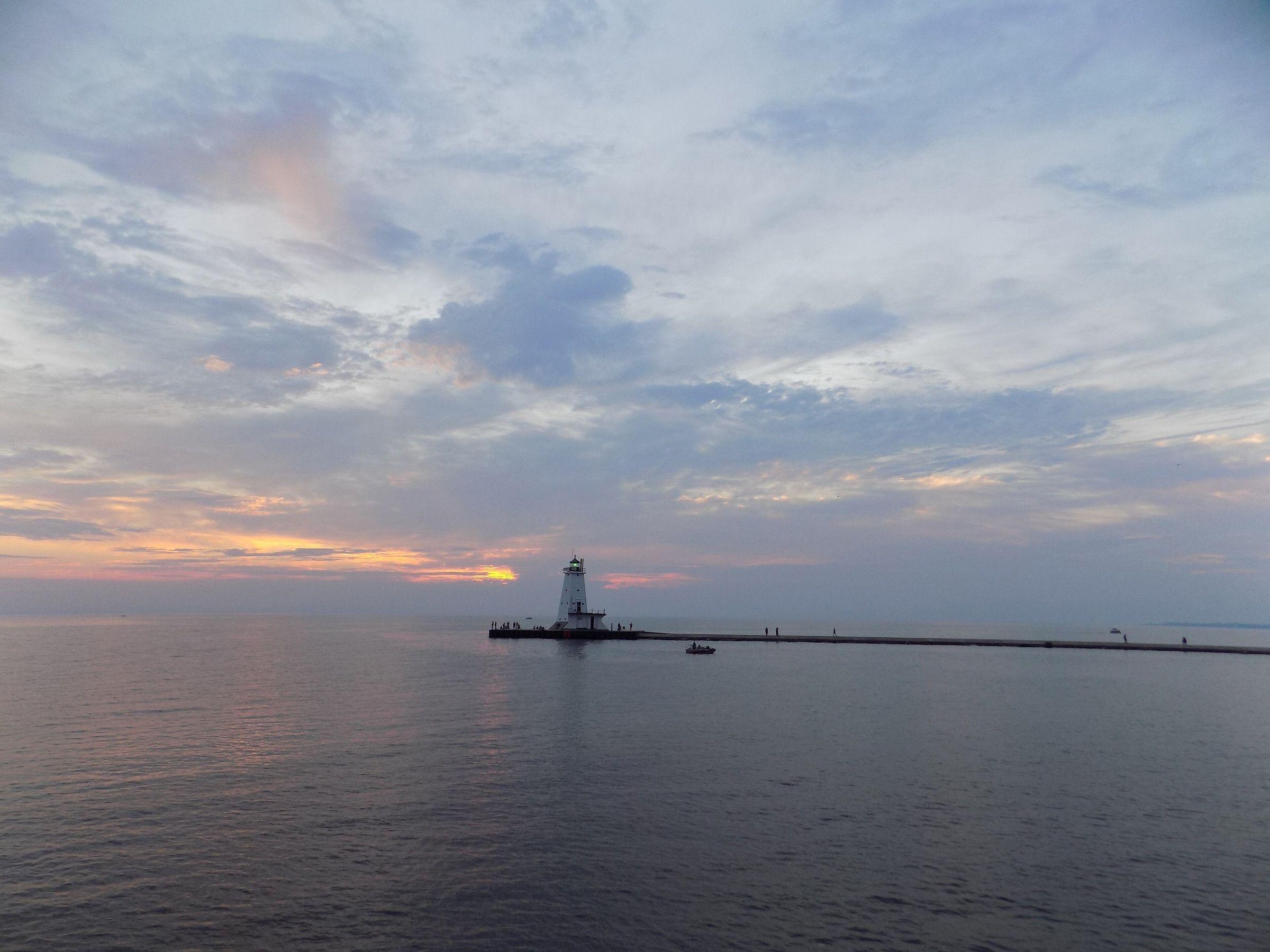 People walking out the Ludington north breakwater toward the lighthouse at dusk on Lake Michigan