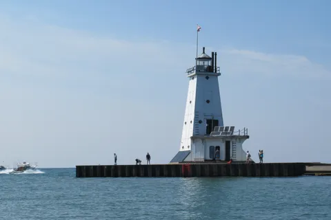 Charter fishing boats heading out past people on the pier at Ludington North Breakwater Light
