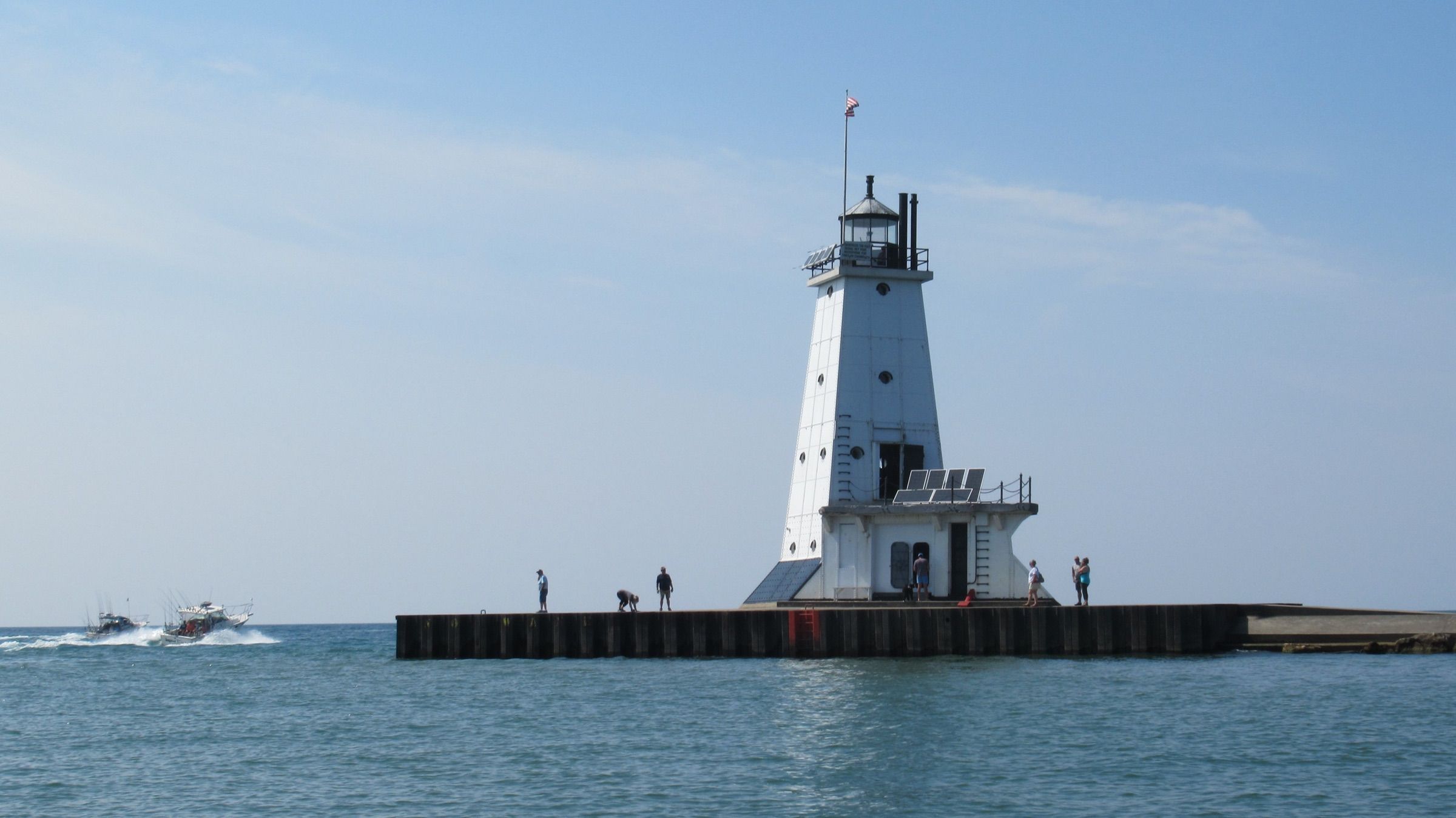 Charter fishing boats heading out past people on the pier at Ludington North Breakwater Light