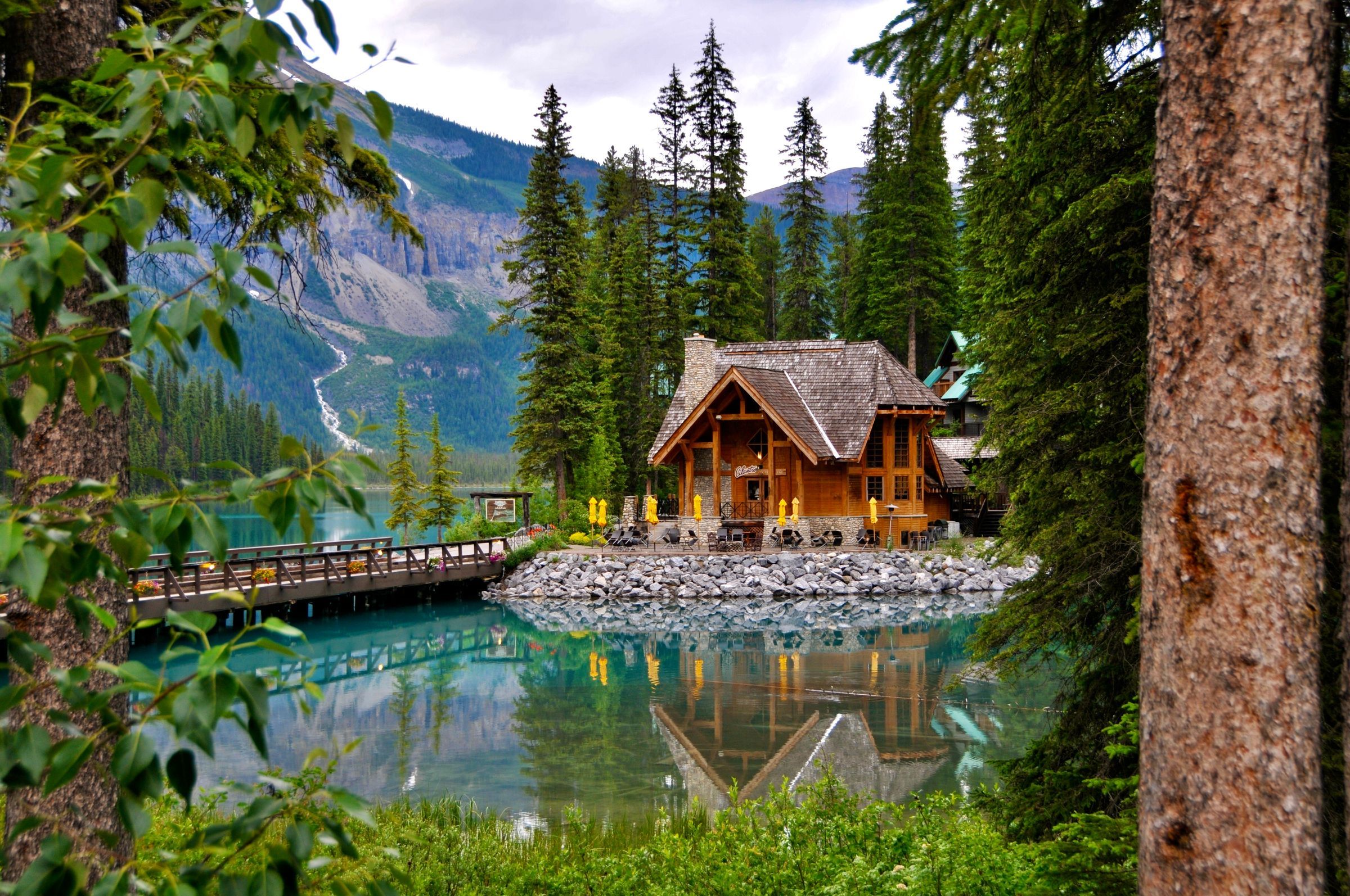 A timber lodge with a stone-walled deck on Emerald Lake, reflected in green water below forested mountains