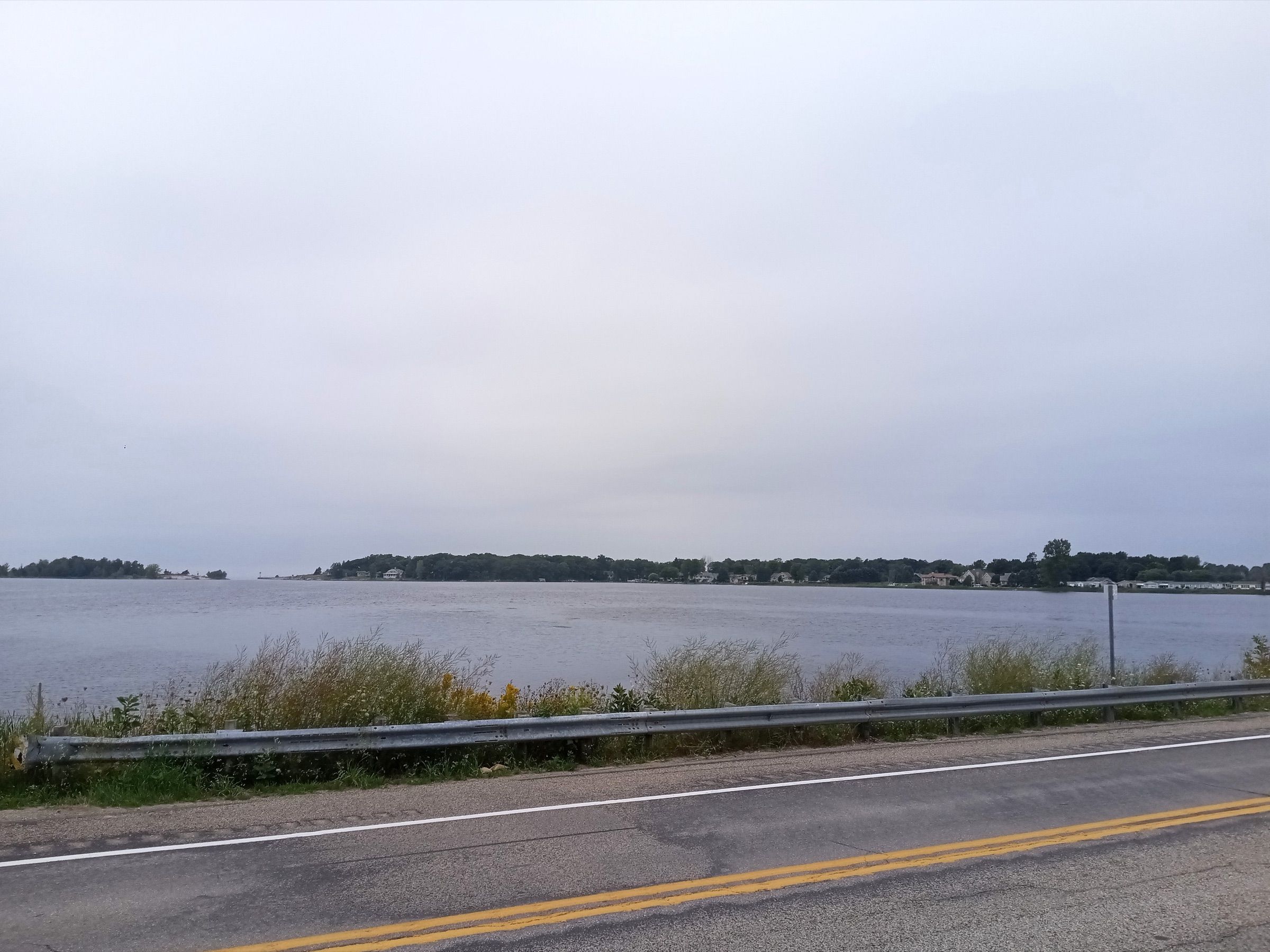 Arcadia Lake under an overcast sky, seen across a roadside guardrail toward the village of Arcadia