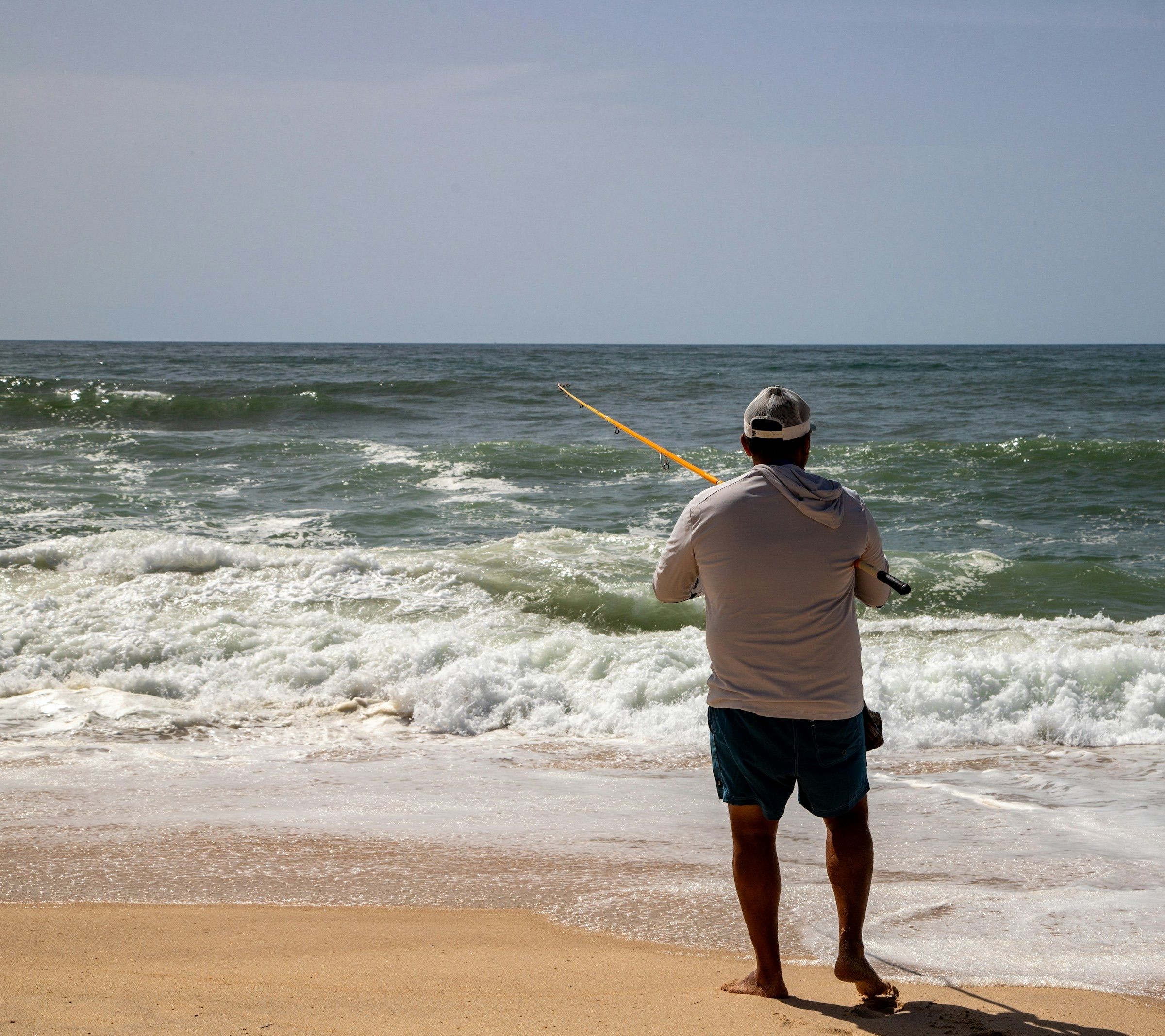 Barefoot angler casting from a sandy beach into breaking surf