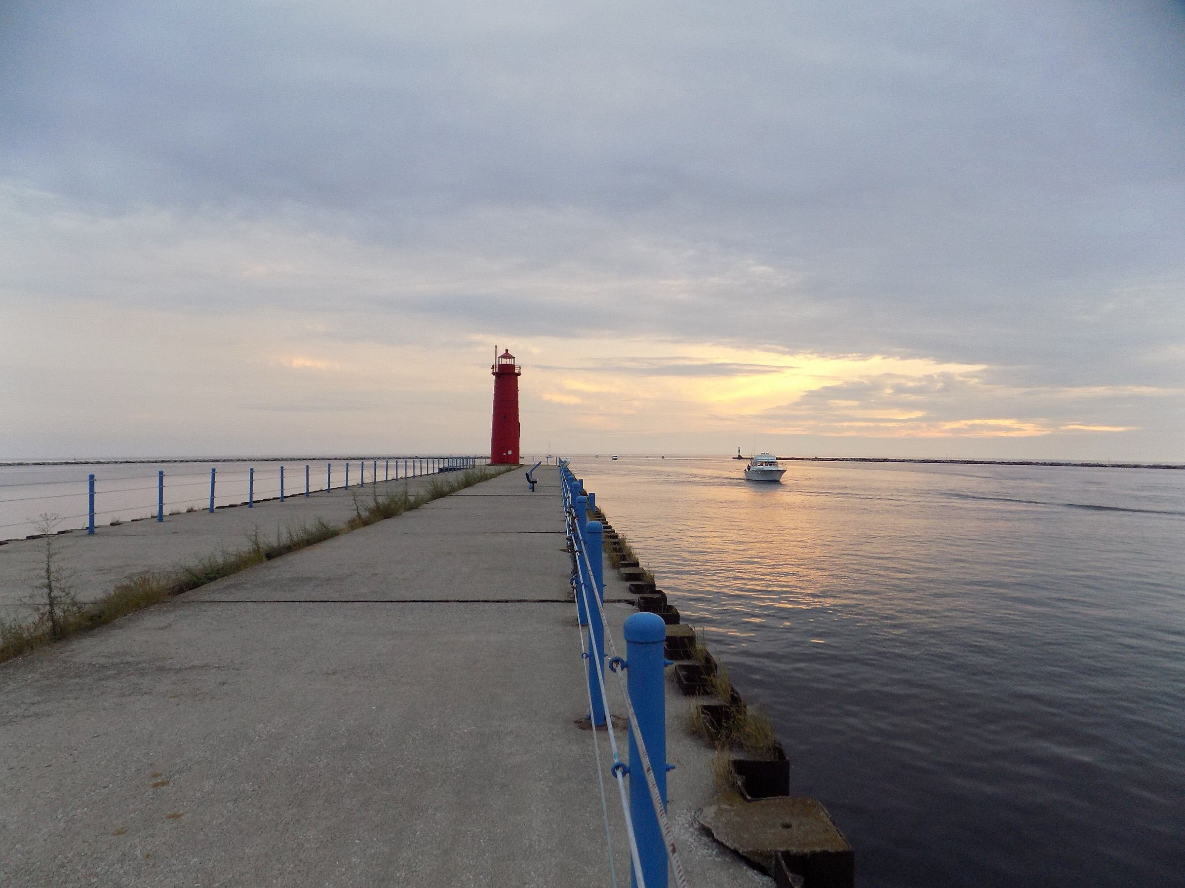 Muskegon pier and red lighthouse on Lake Michigan as a boat heads out at sunset