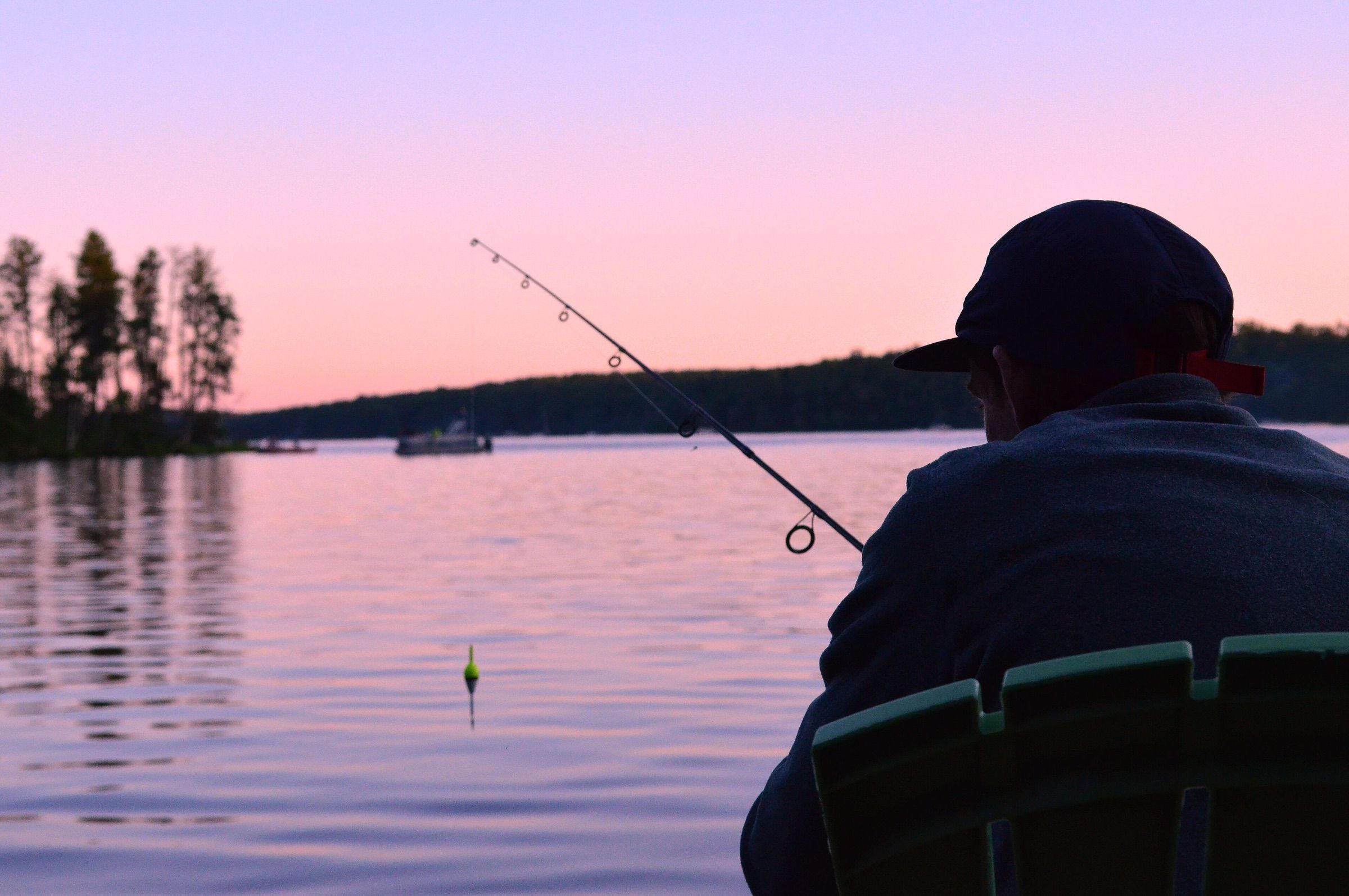 Angler in a cap watching a bobber at dusk while fishing for walleye on a northern lake
