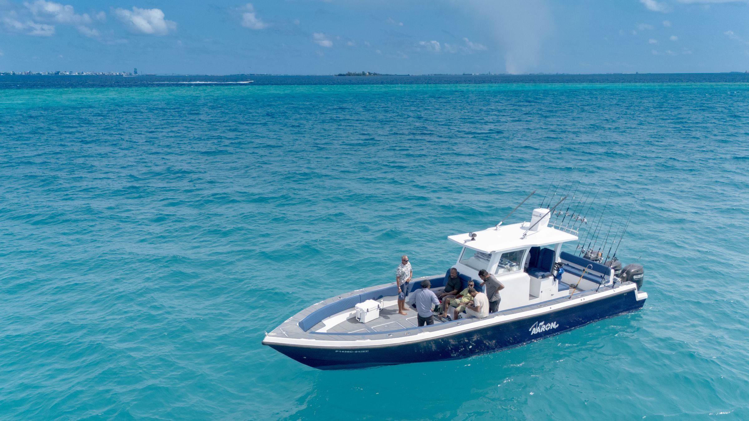 Aerial view of a group of anglers aboard a center-console fishing boat with rods in holders on turquoise water in the Maldives