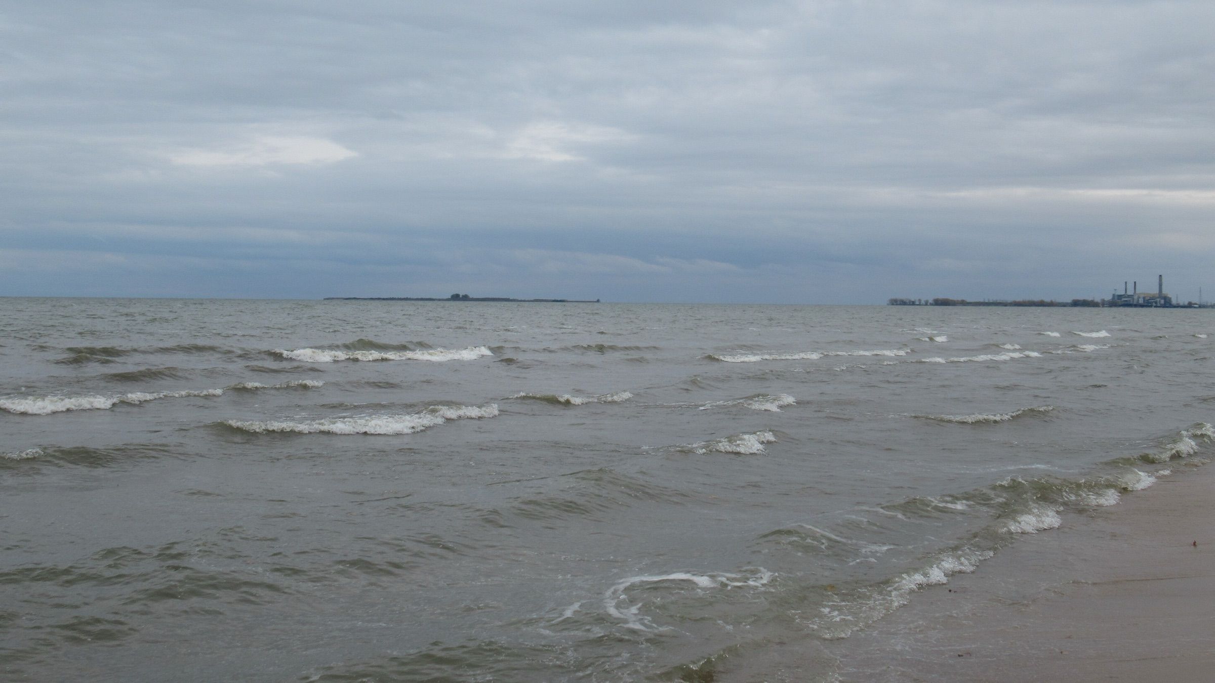 Wind-driven waves roll onto the beach at Bay City State Park under an overcast sky on Saginaw Bay