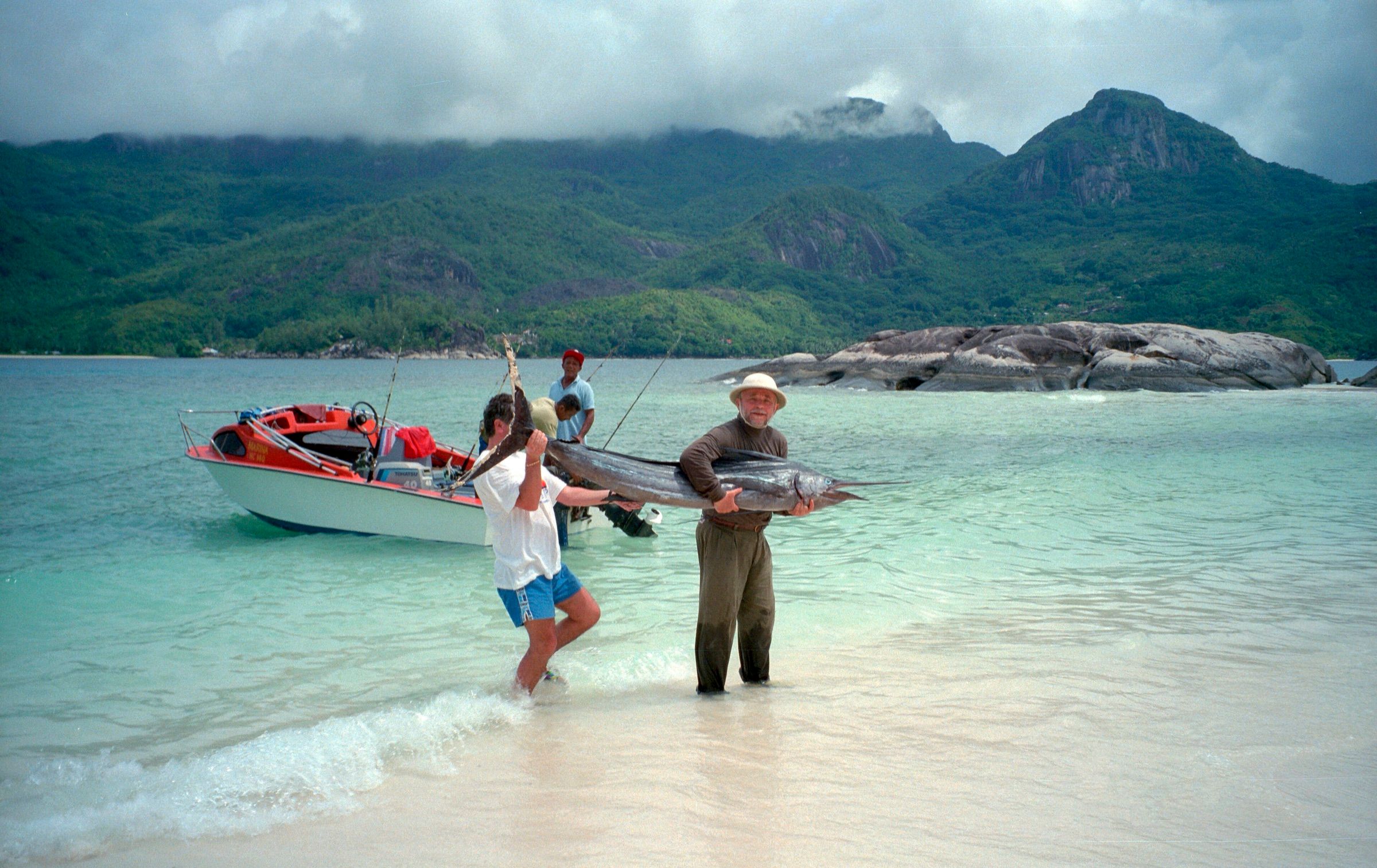 Anglers carrying a sailfish ashore from a small boat in shallow tropical water