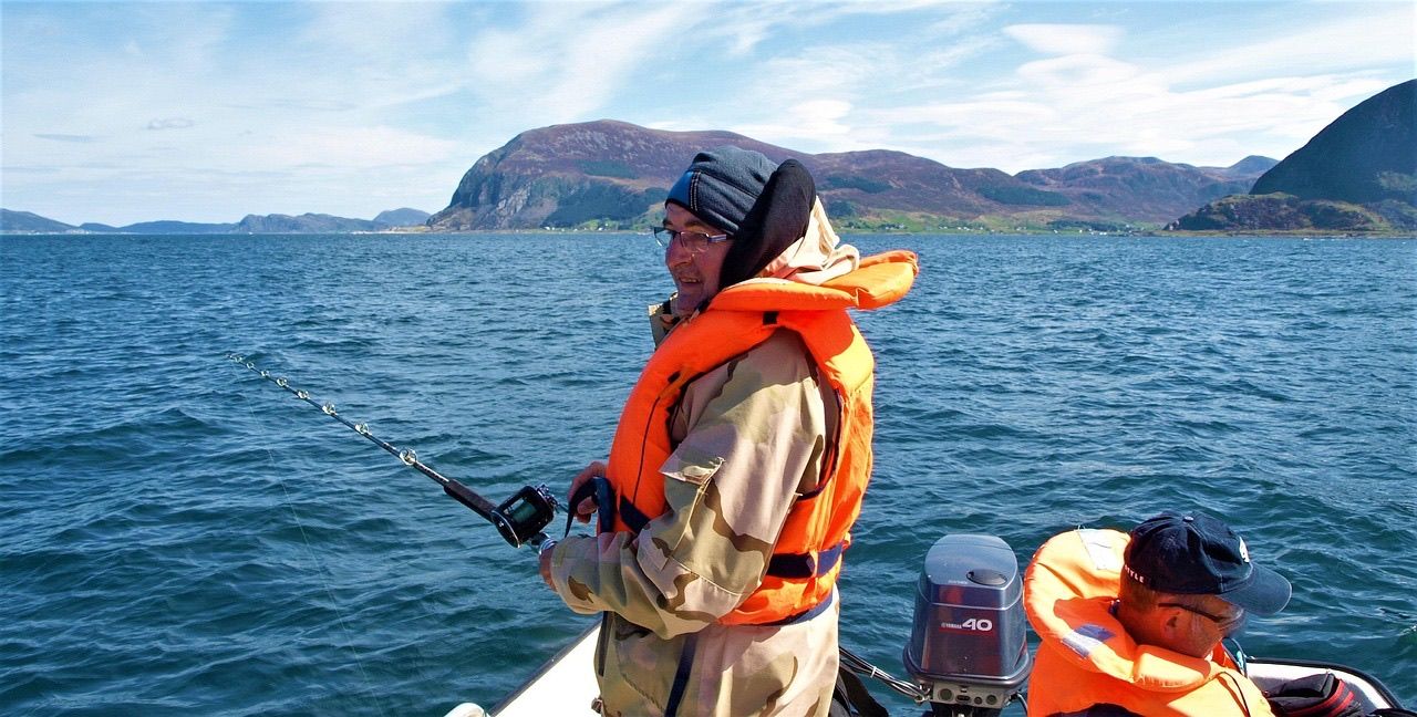 Two anglers in life jackets fishing from a small motorboat on blue sea water below rocky hills