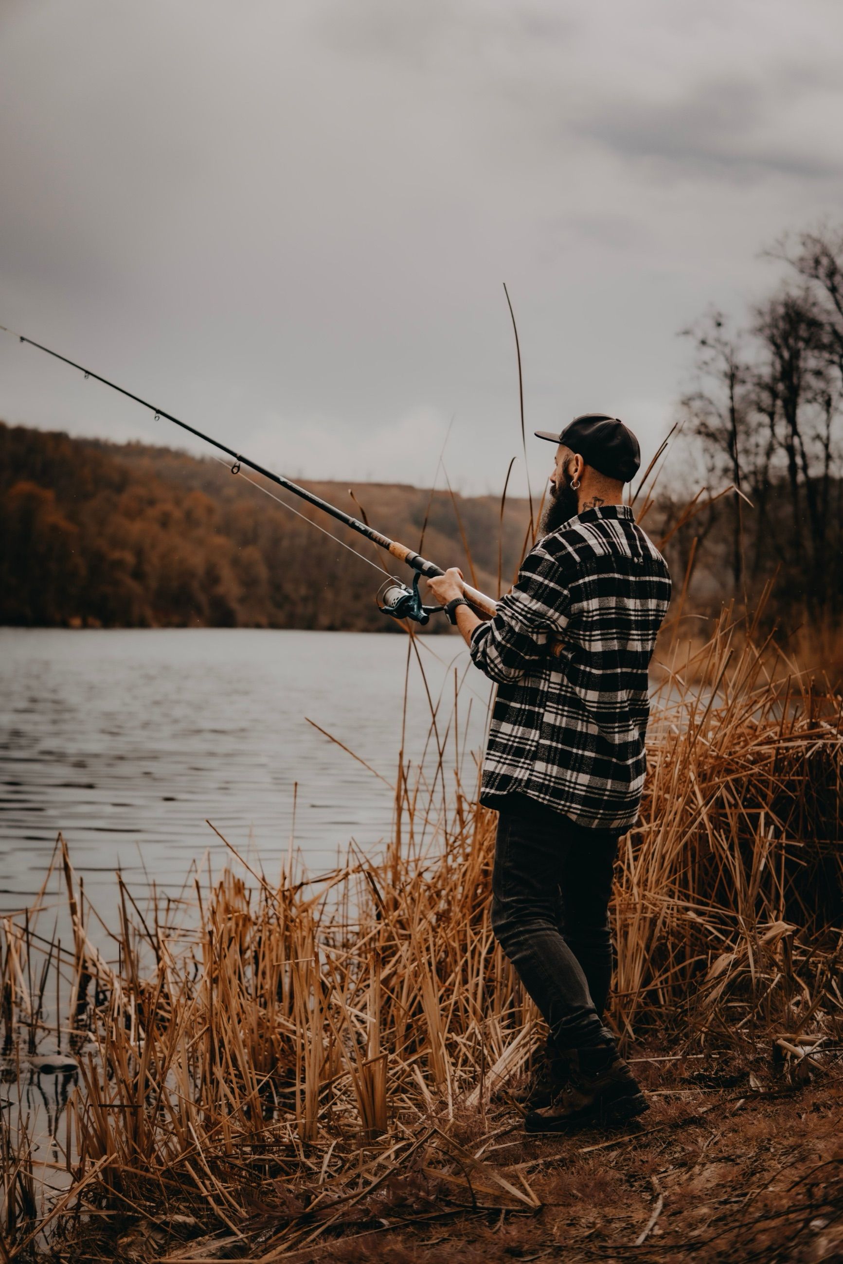 Angler casting from a lakeshore lined with autumn grass and trees