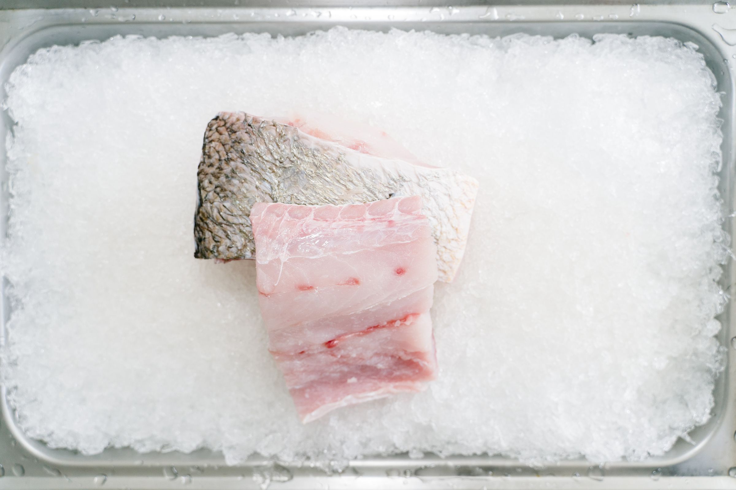 Top view of two skin-on fish fillets on crushed ice in a metal tray