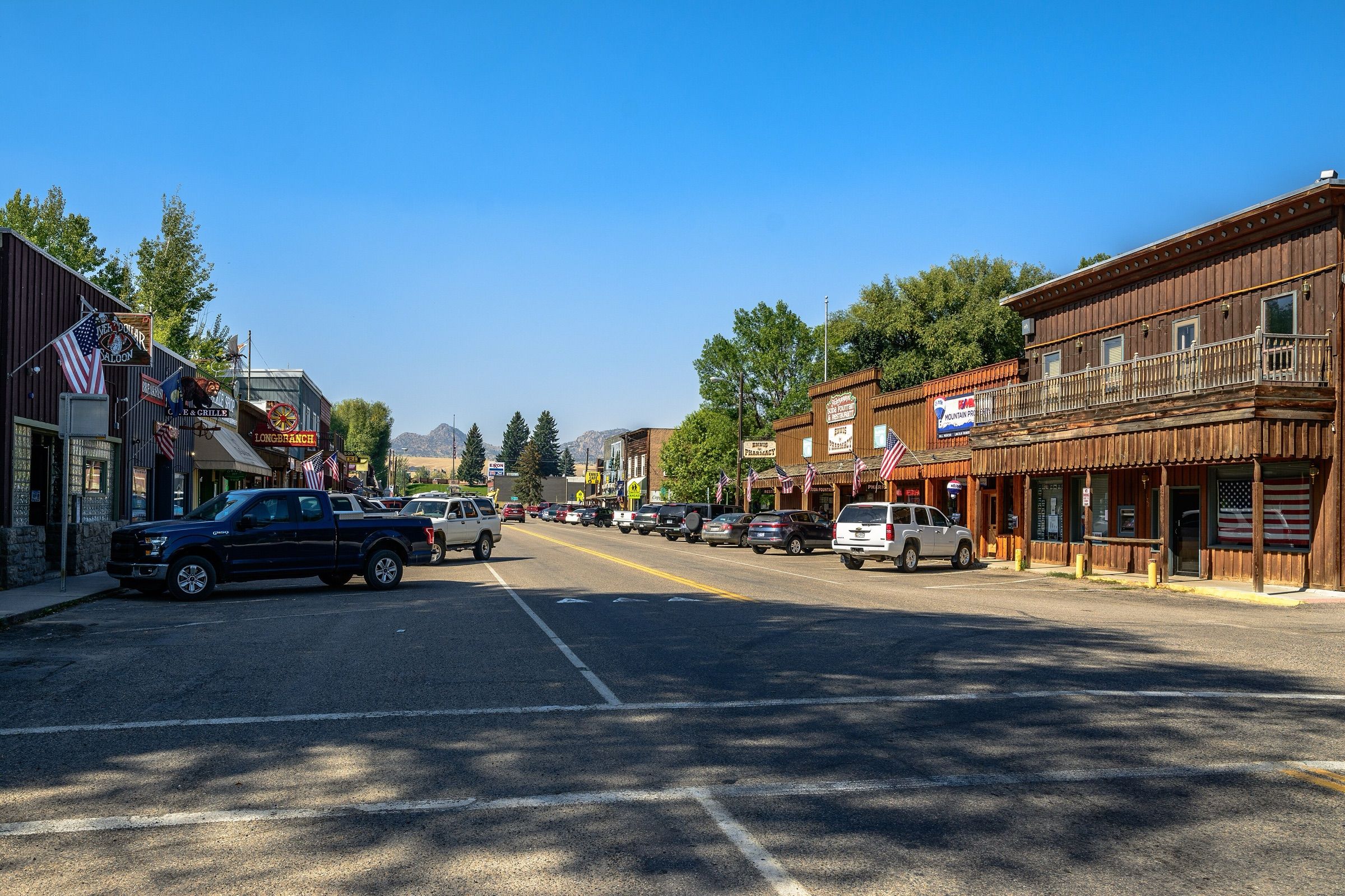 Main street of Ennis with wooden storefronts, pickups and mountains in the distance