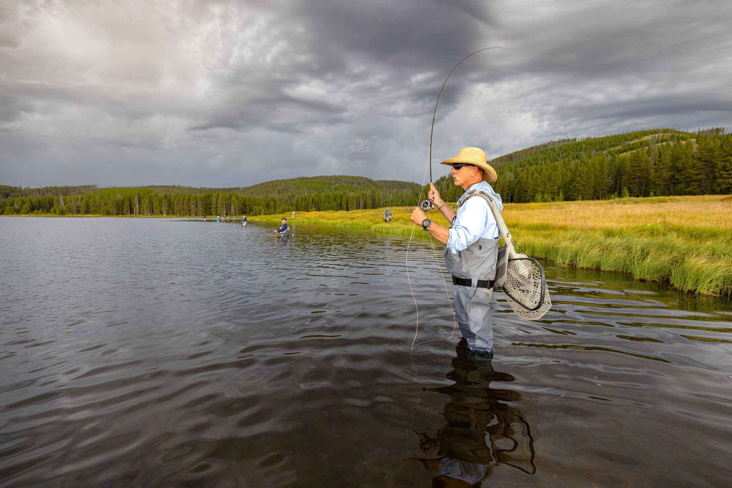 Fly angler wading Grebe Lake in Yellowstone National Park under storm clouds
