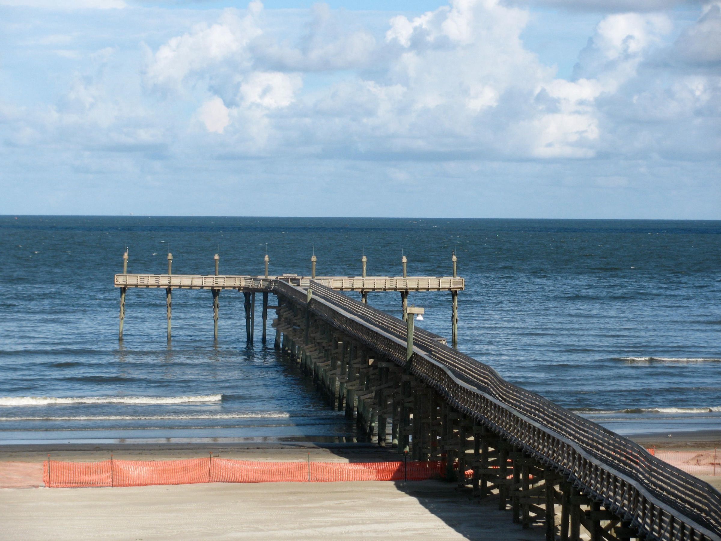 The fishing pier at Grand Isle State Park reaching into the Gulf of Mexico under puffy clouds