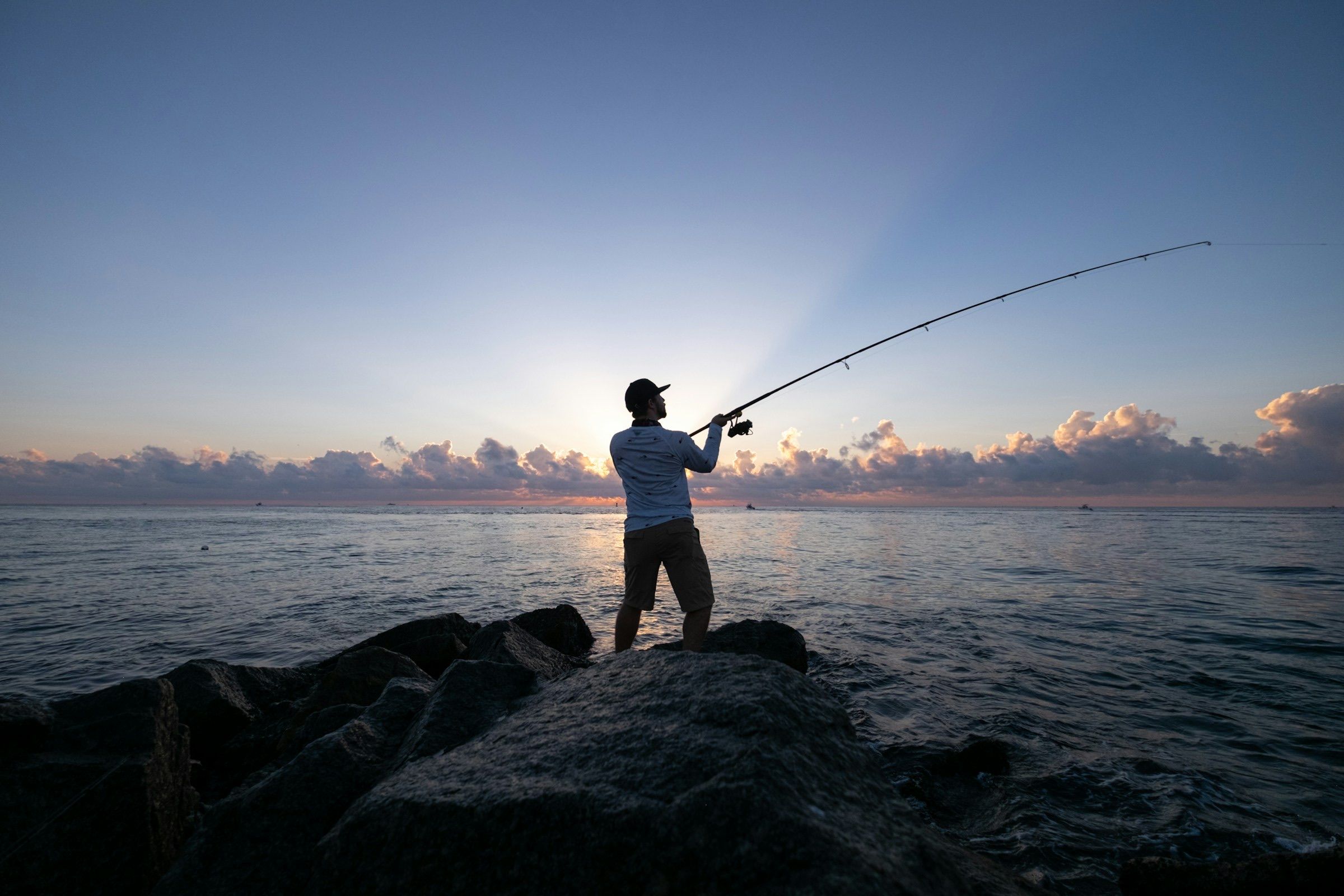 Angler casting from a rock jetty into the Atlantic at sunrise